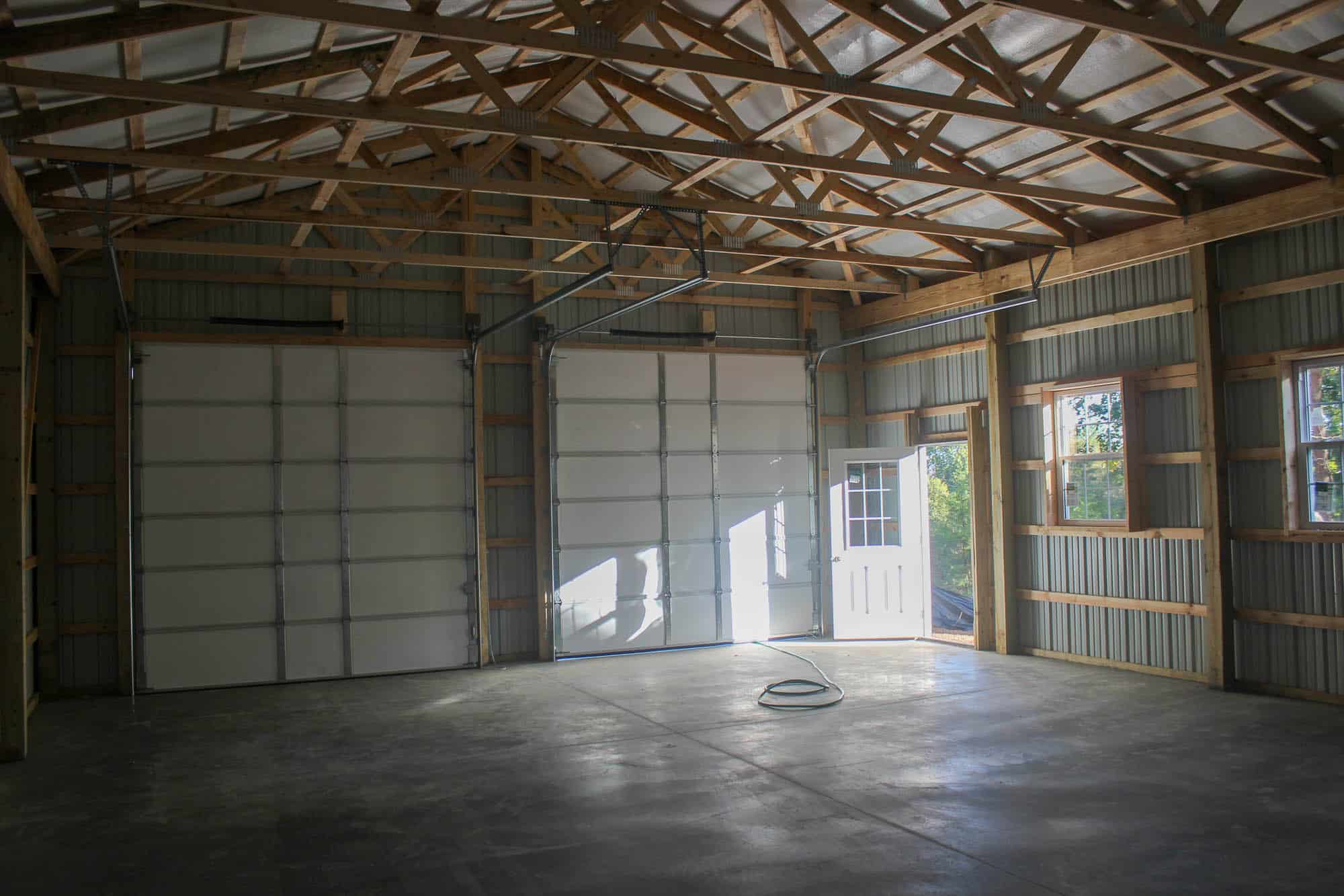 The interior of a red metal garage with exposed wooden framing and metal siding. The ceiling features wooden trusses and the floor is made of concrete.