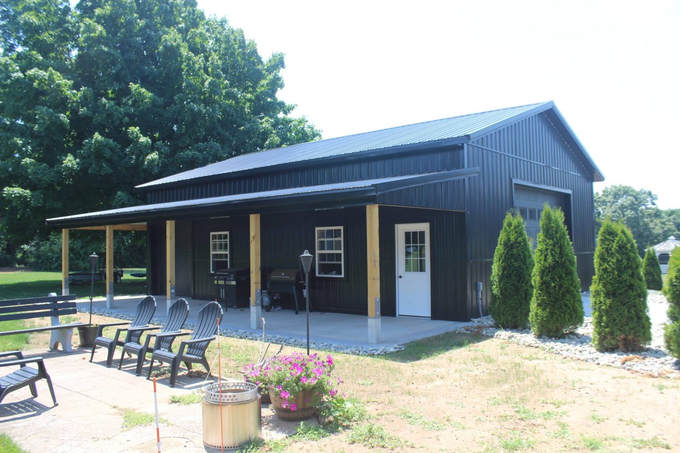 black metal pole barn garage in connecticut with covered porch, white entry door, and outdoor seating area.