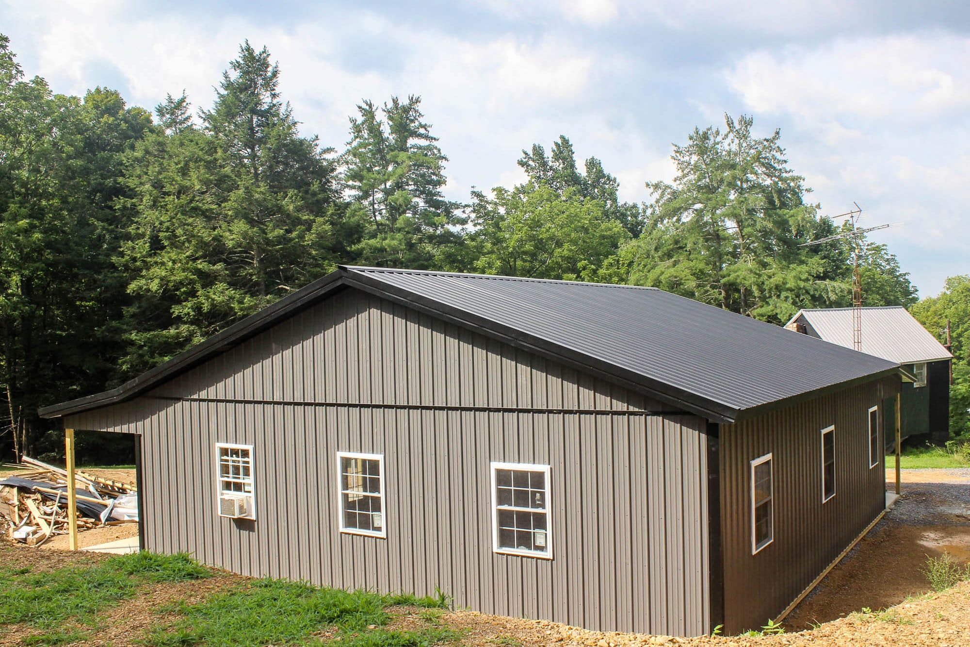a side view of a gray metal building with a black gable roof and multiple white-trimmed windows. the building sits on a gravel foundation.