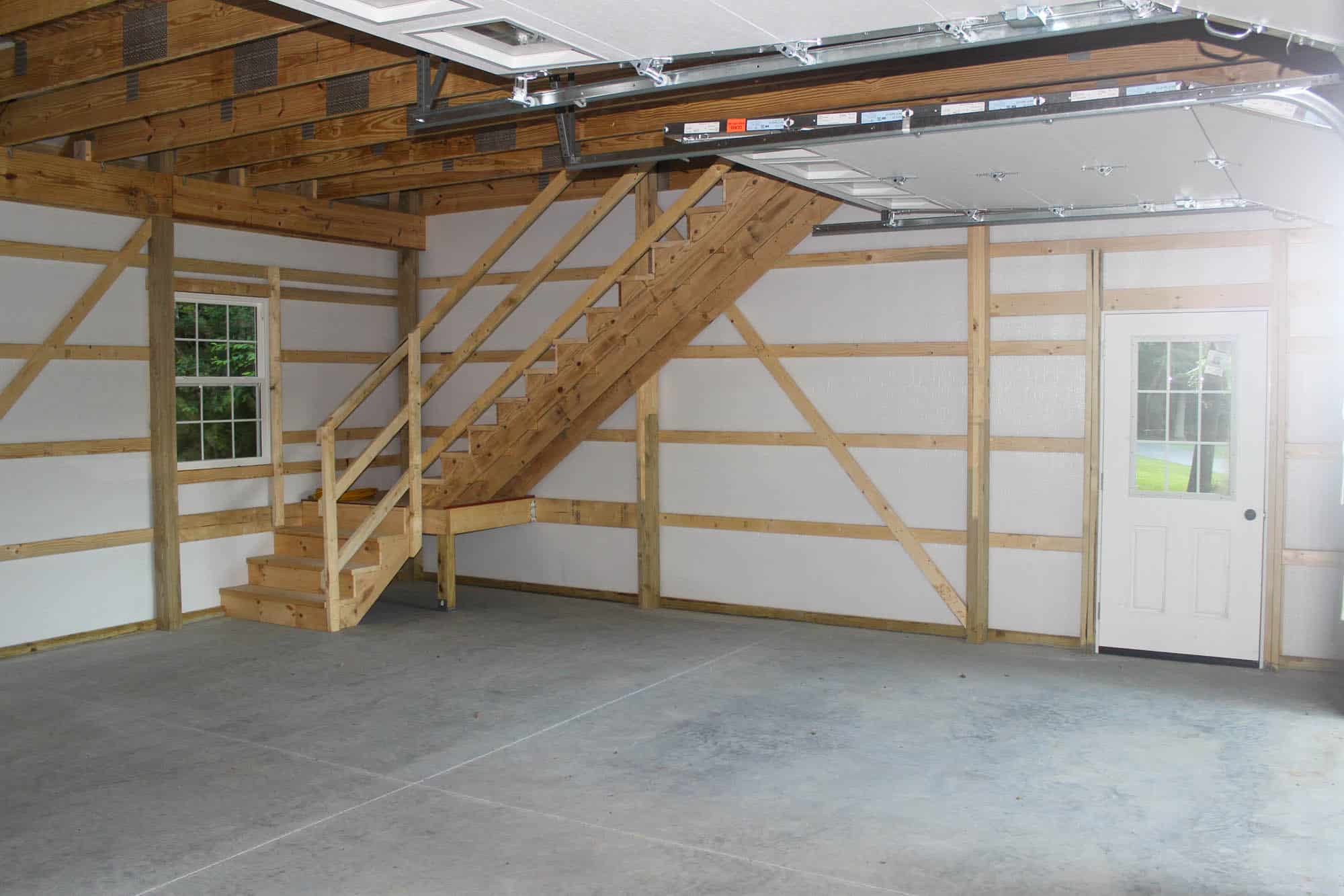 Interior of garage showing a staircase to the upper level, exposed framing, and concrete flooring.