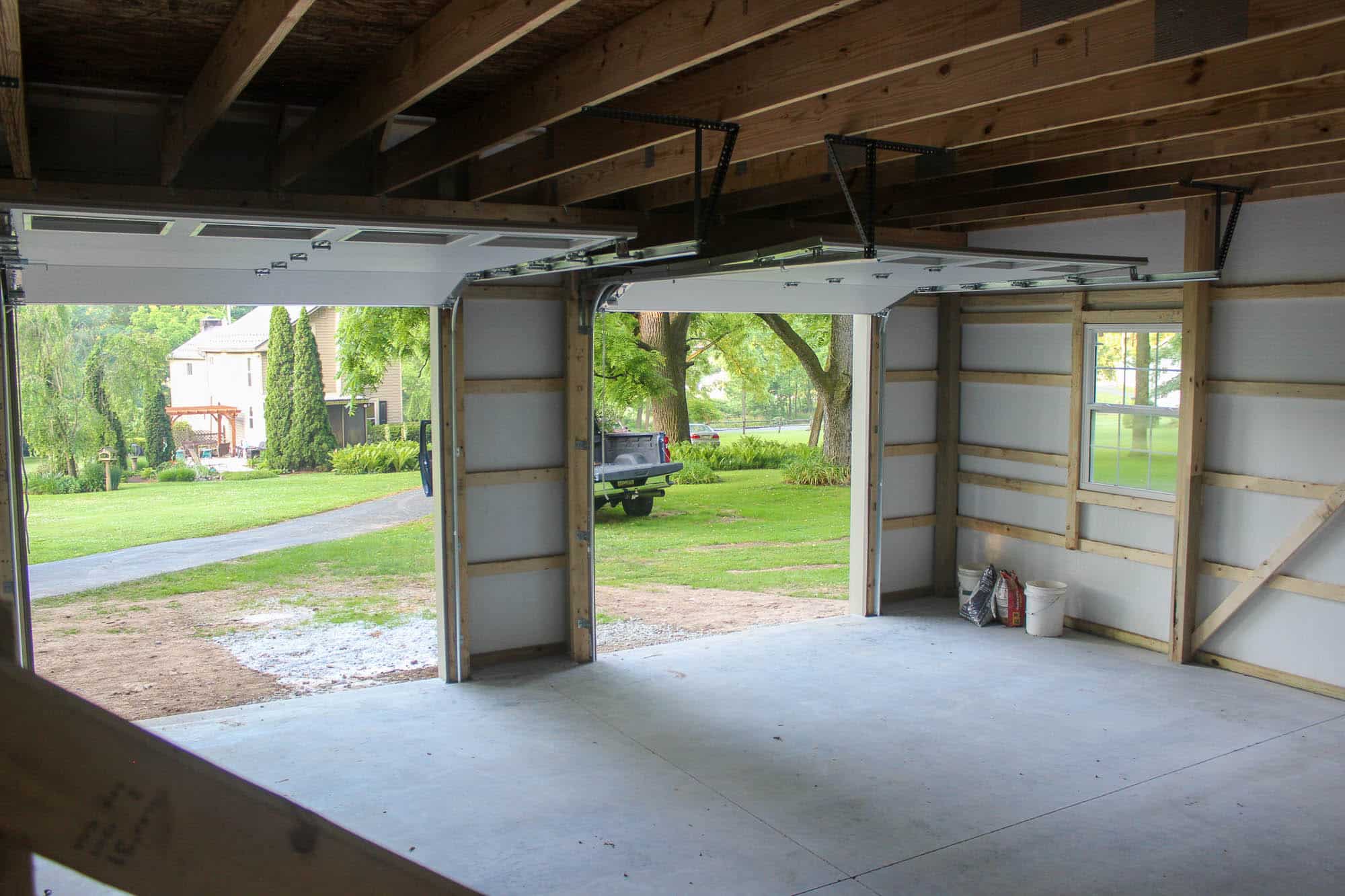 Wide view of a three-bay garage interior with concrete flooring, exposed beams, and natural light entering through the garage doors.