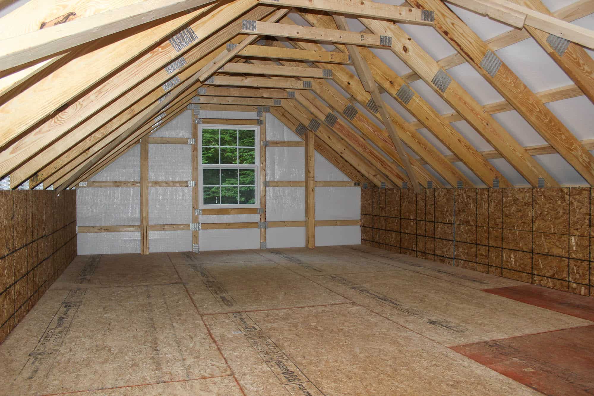 Upstairs loft space inside a garage with wood framing, pitched roof, and windows on both ends for natural light.