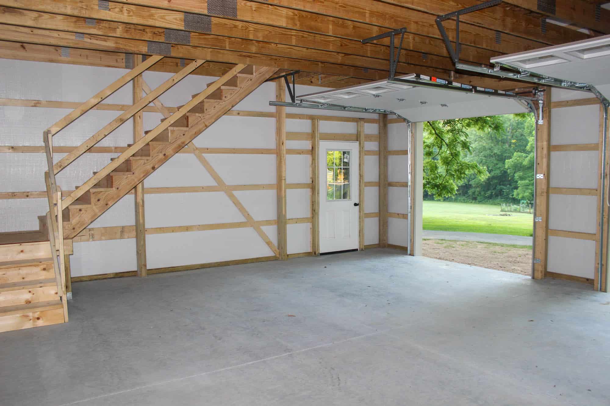 Interior view of a lofted garage with unfinished wood framing and a concrete floor, featuring a staircase to the upper level.