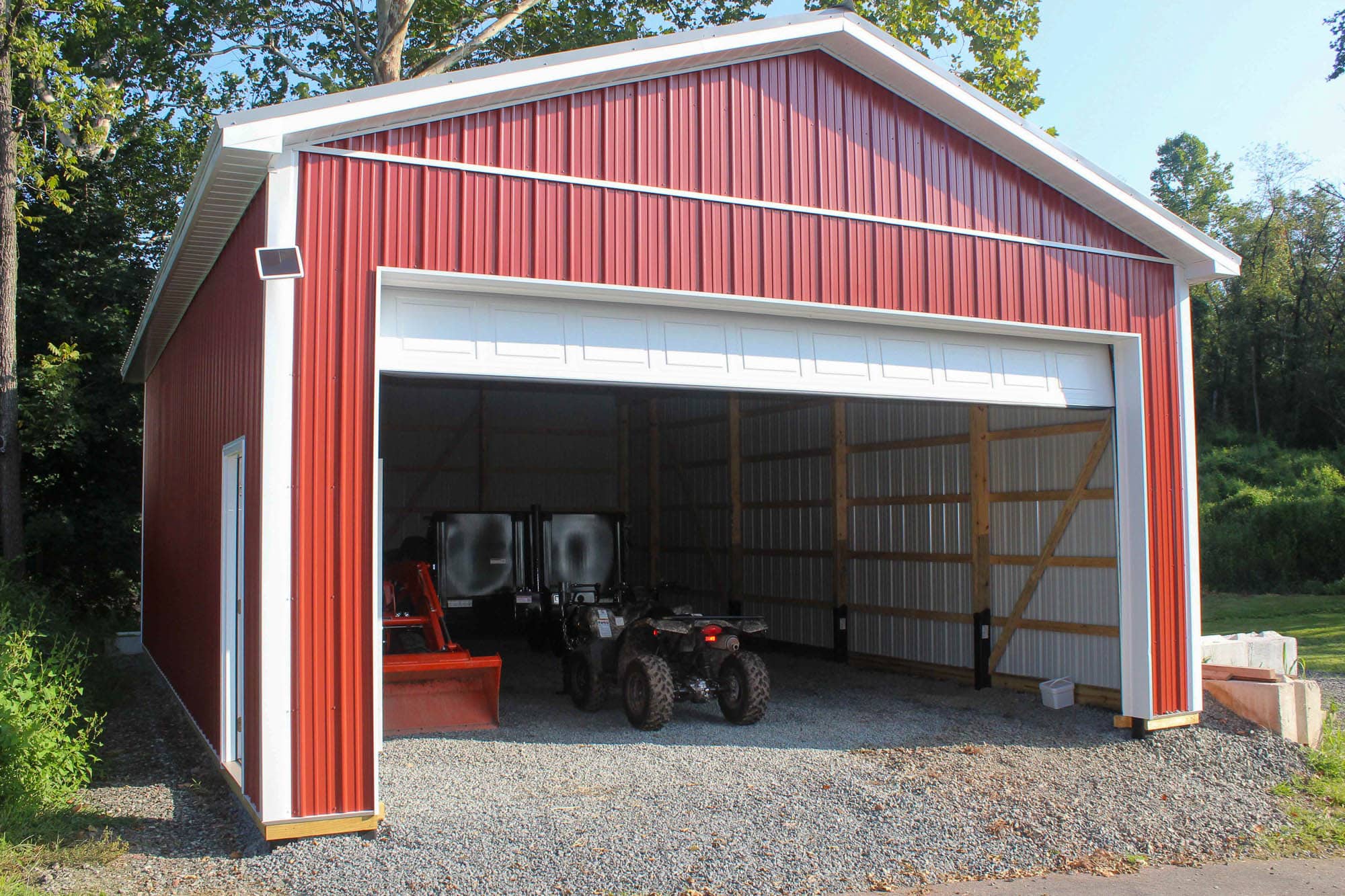 Interior view of a red garage with exposed wood framing, gravel floor, and lawn mowers stored inside.