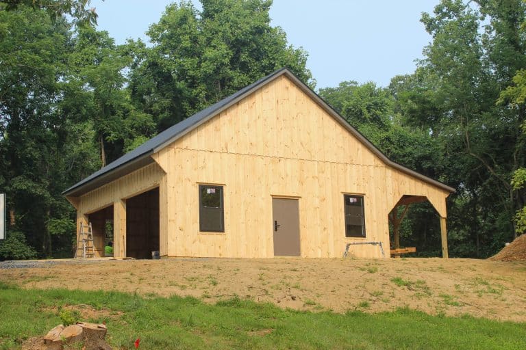 completed twin-door wood garage viewed from the front lawn, framed by trees and a vehicle parked nearby.
