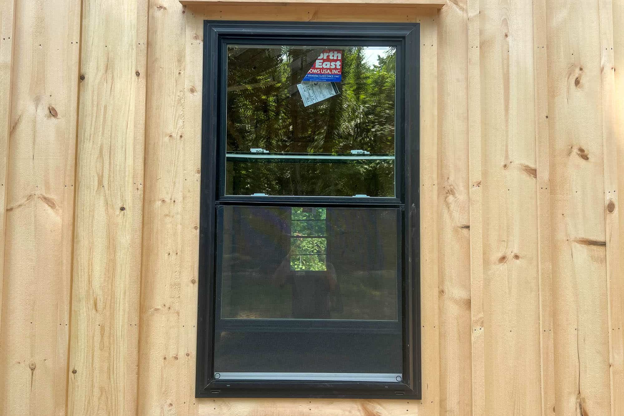 Side view of a light wood garage with a wide covered porch area supported by timber posts, located in a wooded area.