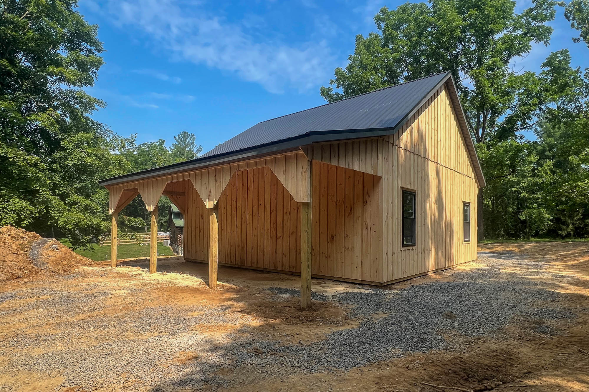 Angled view of a timber garage with a deep covered porch entry and finished wood siding, surrounded by forest.