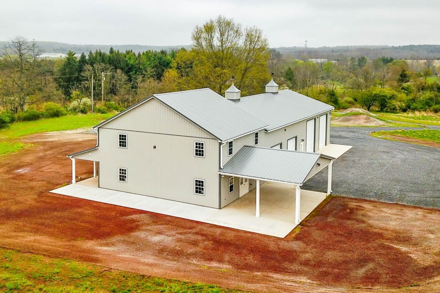aerial view of a large beige post-frame building with metal roofing, cupolas, garage bays, and covered entry areas.