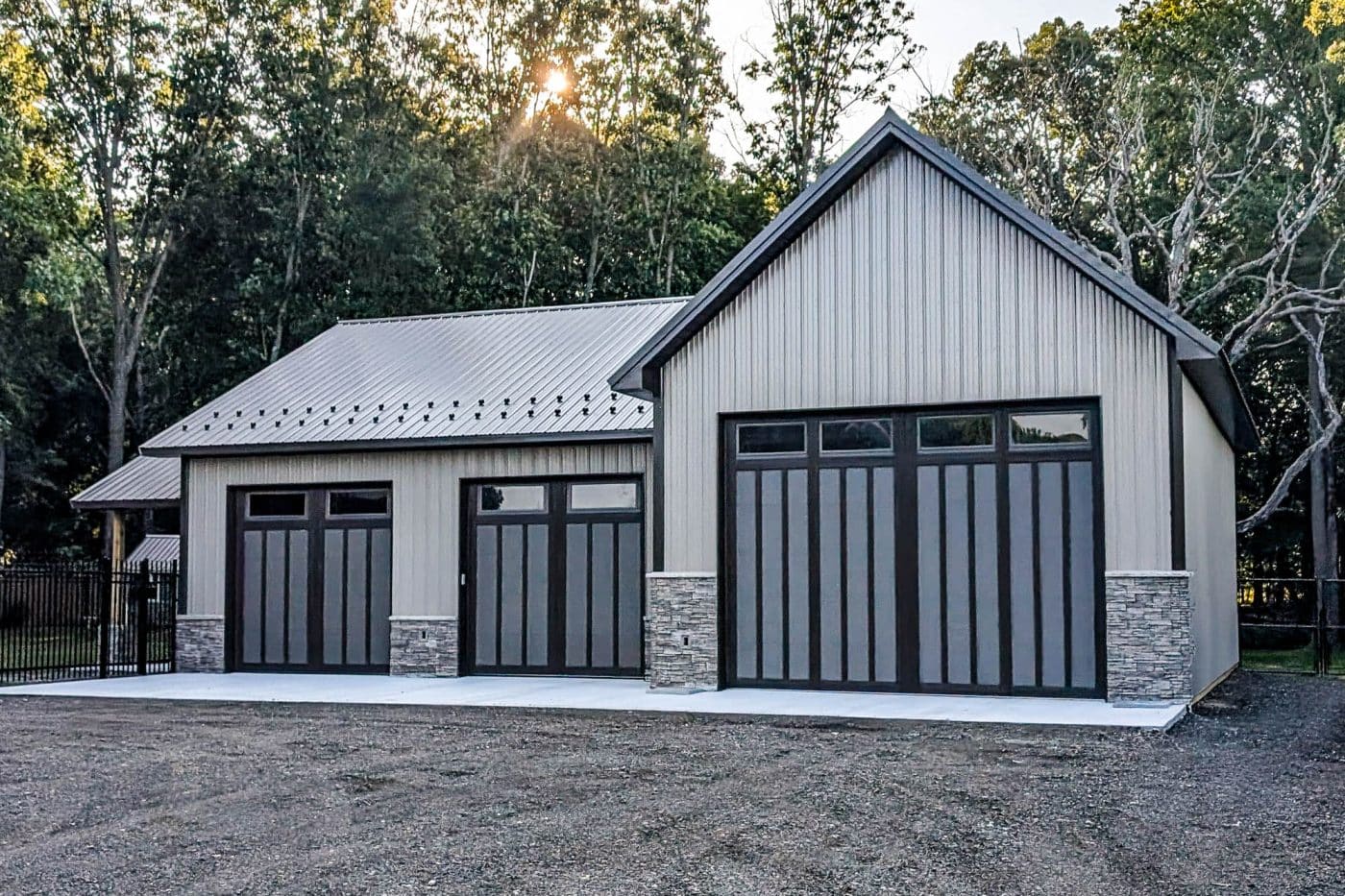 beige pole barn garage with three black overhead doors and stone accents.