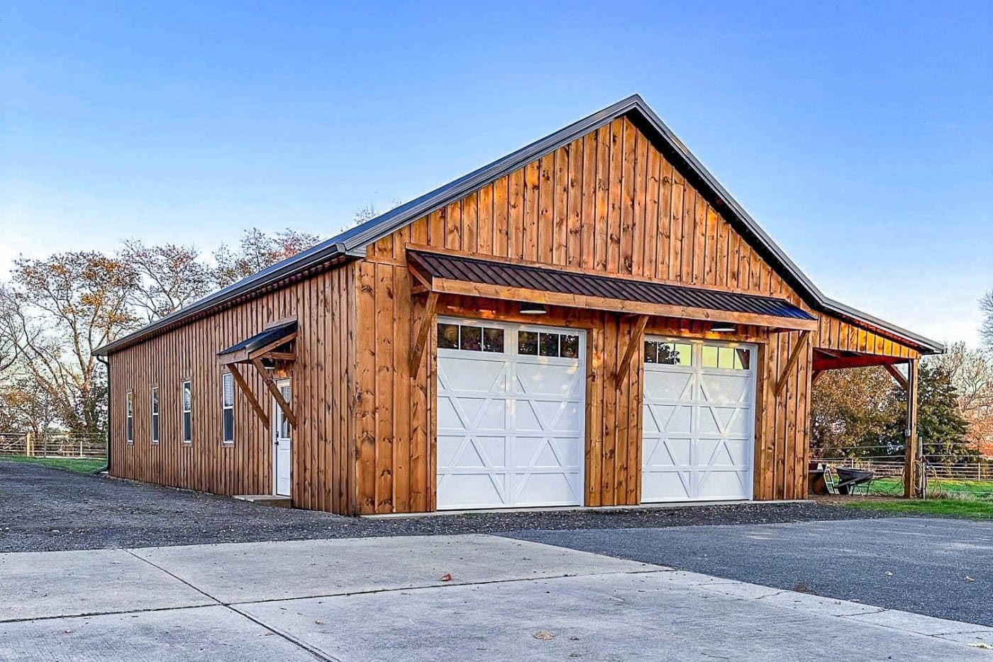 wood-sided pole barn garage with two white overhead doors and covered side area.