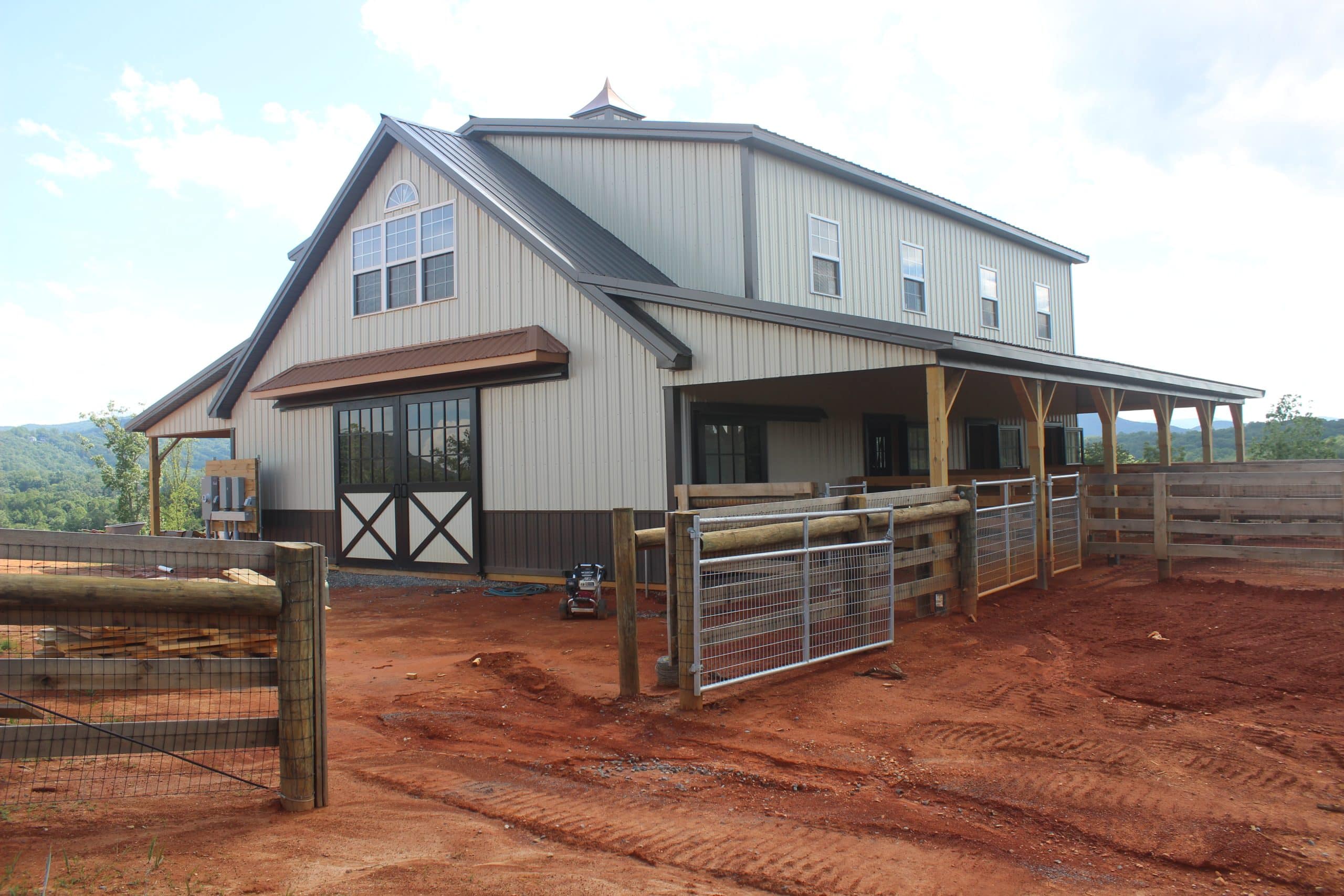 large horse barn with covered areas, sliding doors, and fenced paddocks