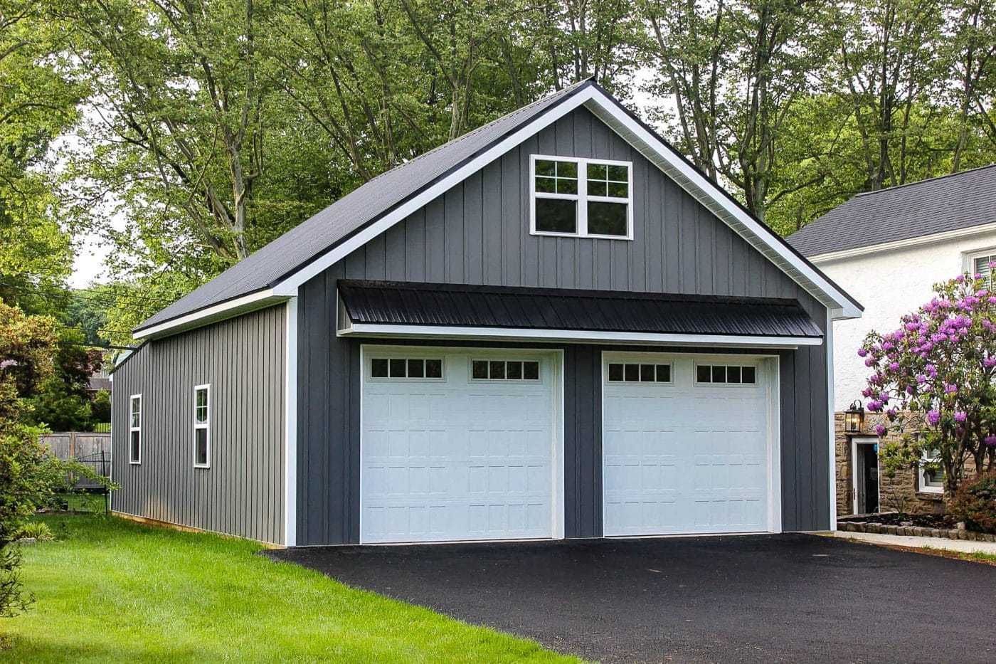 gray post-frame garage with two white overhead doors, black metal awning, and white trim.