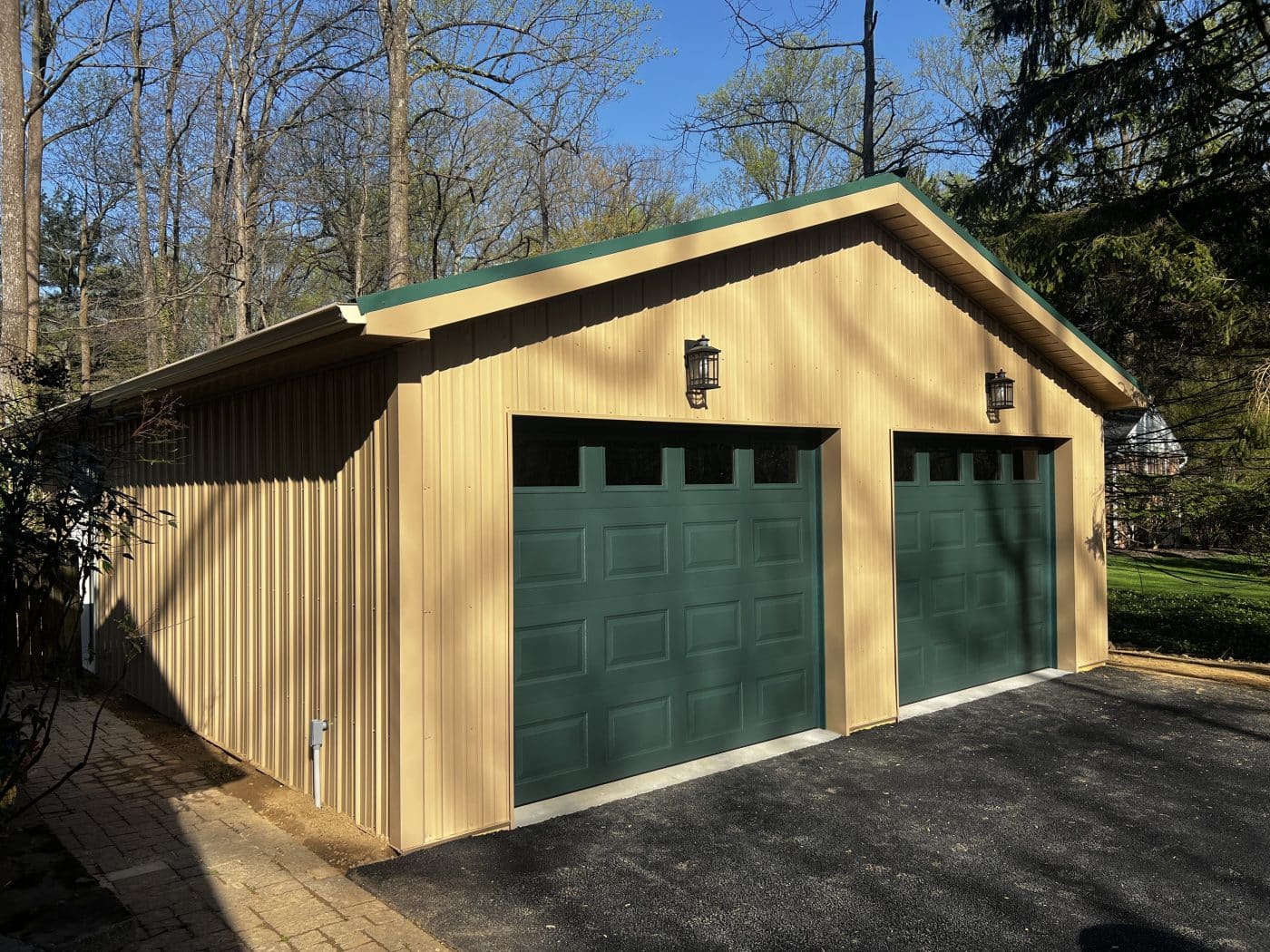 wo green overhead garage doors installed on a tan post-frame garage building.