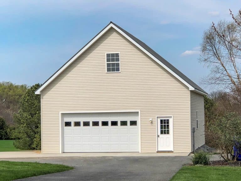 beige pole barn garage in new jersey with a white overhead door, side entry door, and paved driveway.