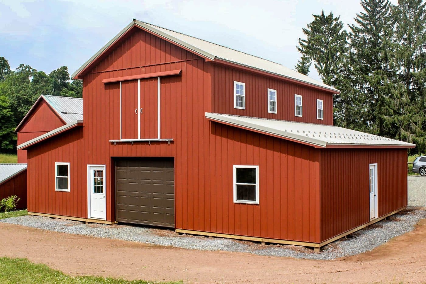 red pole barn with metal roof, brown overhead garage door, white entry doors, and multiple windows.