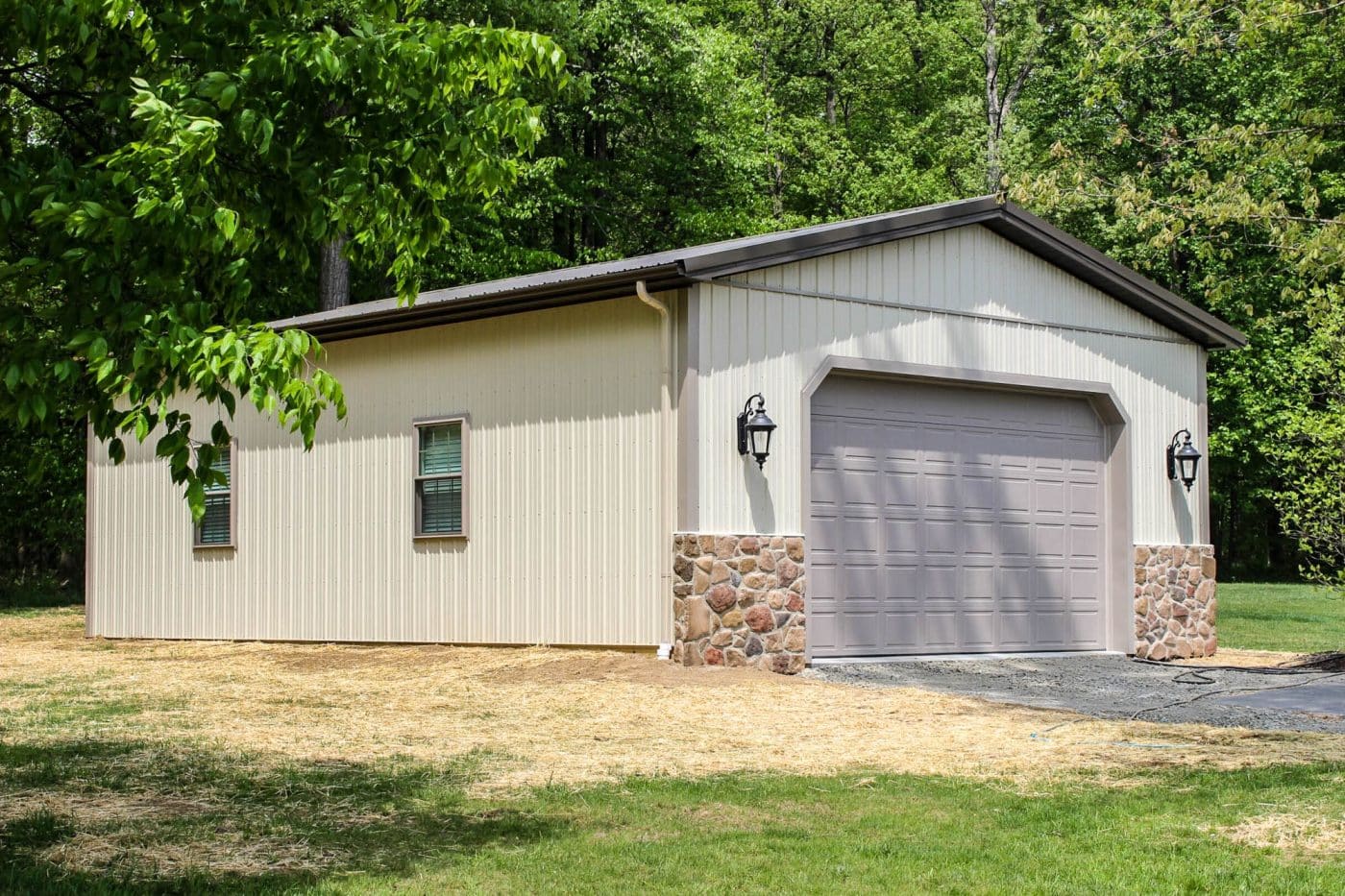 beige pole barn garage with three black overhead doors and stone accents.